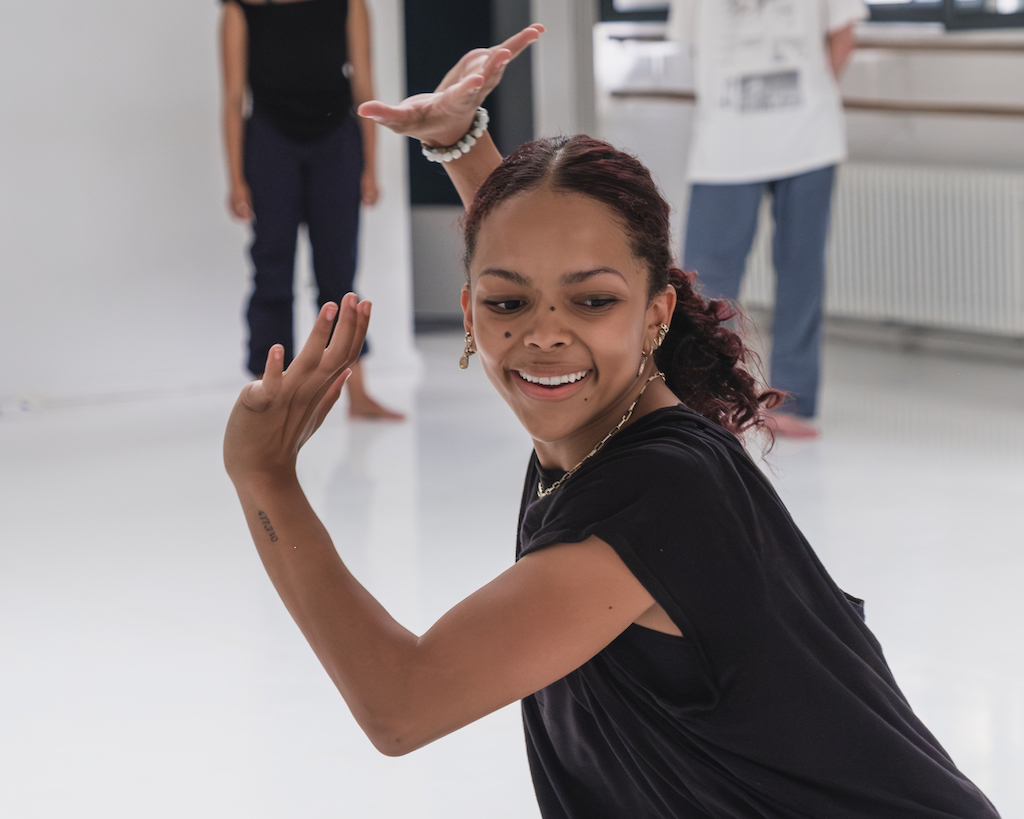 Dancer smiles as she poses her arms to the left of the photo